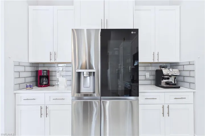 Kitchen featuring stainless steel fridge, white cabinets, backsplash, and light stone countertops