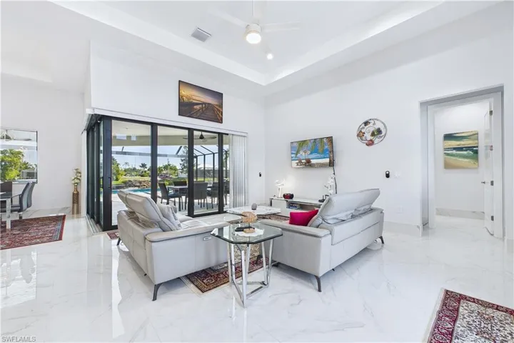 Living room with light marble finish floors, a high tray ceiling, and ceiling fan