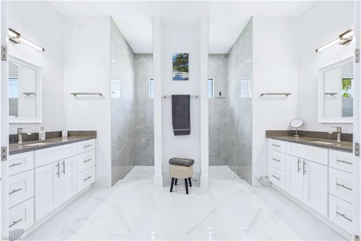 Full bathroom featuring a marble finish shower, two vanities, and healthy amount of natural light