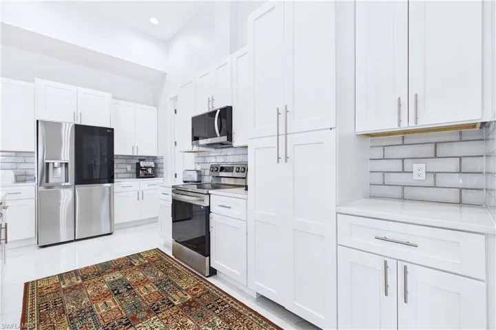 Kitchen featuring stainless steel appliances, white cabinets, decorative backsplash, light stone counters, and recessed lighting