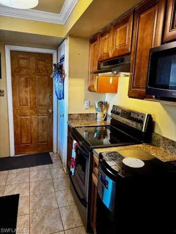Kitchen featuring stainless steel electric range oven, brown cabinetry, black microwave, crown molding, and light tile patterned floors