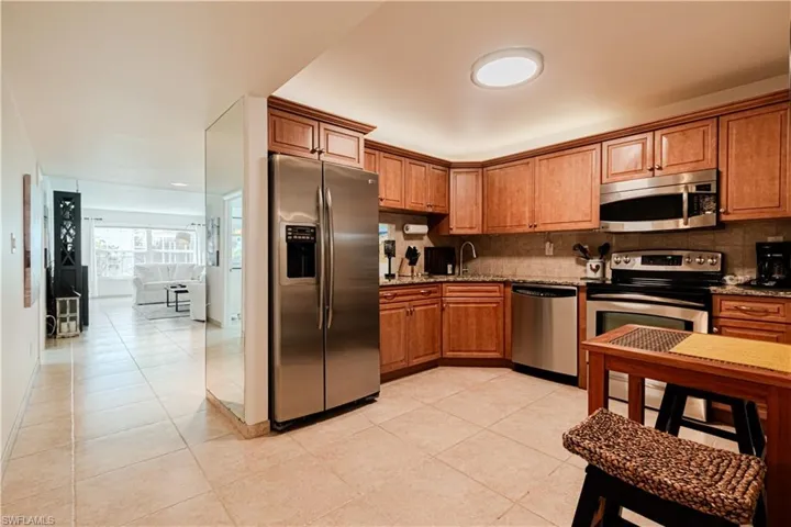 Kitchen with stainless steel appliances, light stone countertops, wood finish cabinetry, light tile patterned floors, and tasteful backsplash