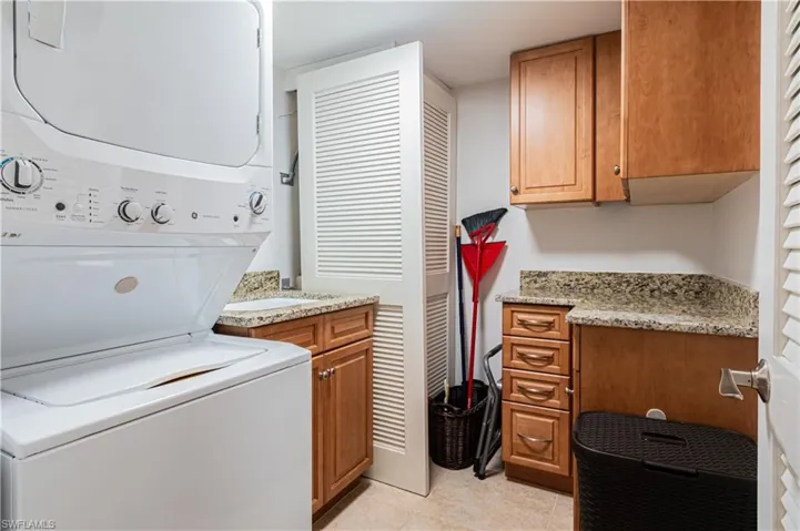 Laundry room with stacked washing machine and dryer, light tile patterned floors, and cabinet space