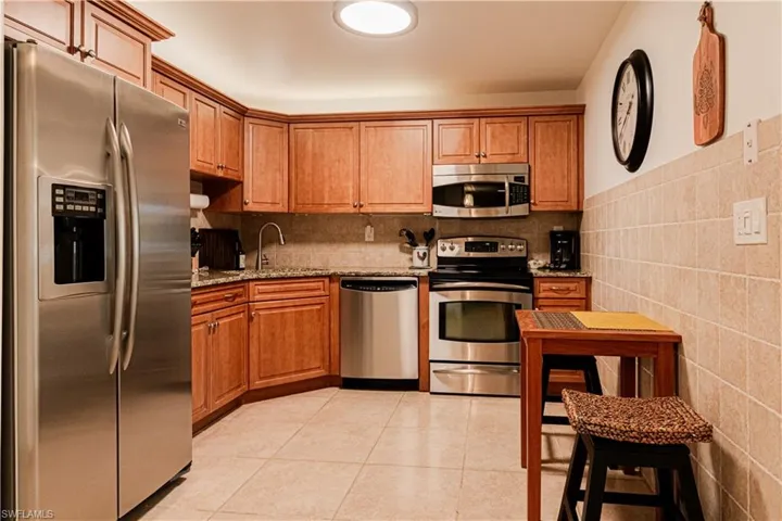 Kitchen with stainless steel appliances, light stone counters, light tile patterned flooring, and wood finish cabinetry