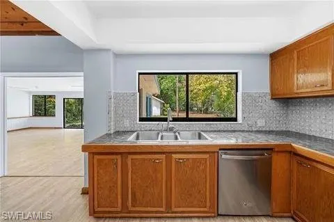 Kitchen with brown cabinetry, stainless steel dishwasher, tasteful backsplash, and plenty of natural light