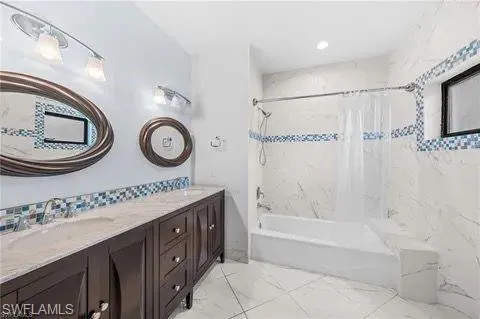 Bathroom featuring shower / bath combo, double vanity, and light marble finish floors