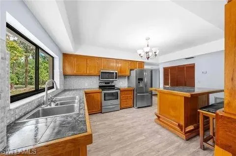 Kitchen with stainless steel appliances, brown cabinets, a chandelier, light wood-type flooring, and backsplash
