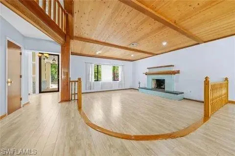 Unfurnished living room featuring light wood-style flooring, wood ceiling, and a fireplace with raised hearth