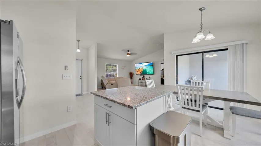 Kitchen with stainless steel fridge, decorative light fixtures, light stone counters, vaulted ceiling, and a center island