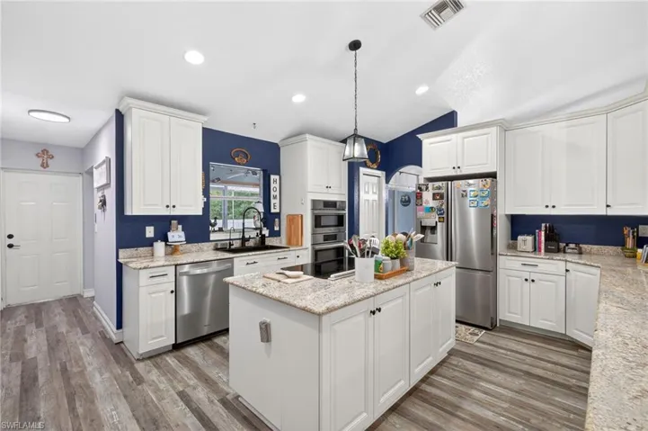 Kitchen with white cabinetry, stainless steel appliances, a kitchen island, light stone countertops, and light wood-type flooring
