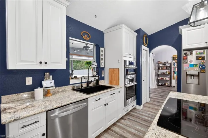 Kitchen with white cabinetry, stainless steel appliances, light wood-style floors, arched walkways, and a textured wall