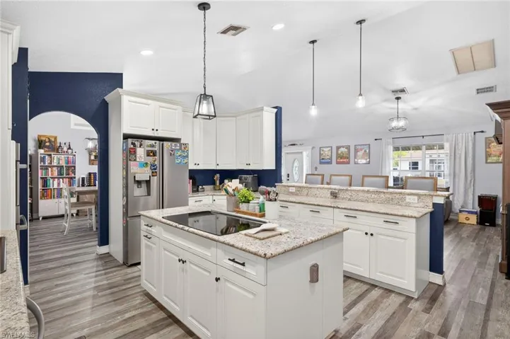 Kitchen with white cabinets, a peninsula, light stone countertops, decorative light fixtures, and vaulted ceiling