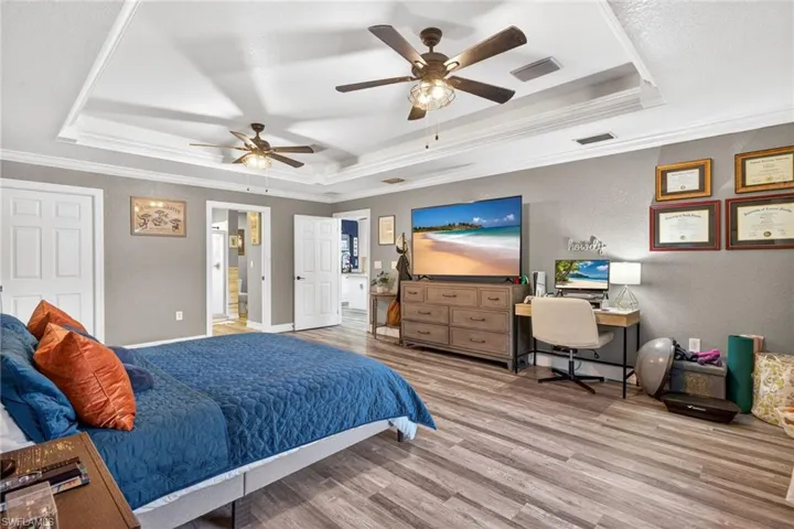 Primary Bedroom featuring ornamental molding, a textured wall, light wood finished floors, a raised ceiling, and ceiling fan