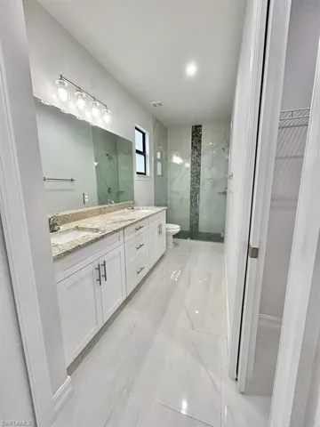 Full bathroom featuring double vanity, a marble finish shower, a spacious closet, light marble finish floors, and recessed lighting