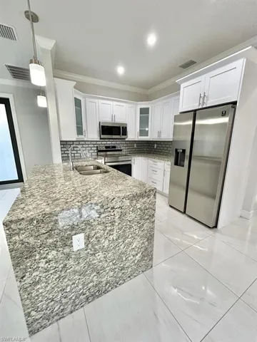 Kitchen featuring glass insert cabinets, crown molding, stainless steel appliances, light stone counters, and white cabinetry