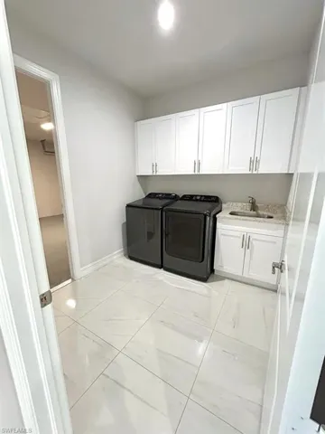 Laundry room featuring cabinet space, washing machine and clothes dryer, and light marble finish floors