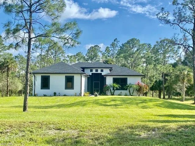 View of front of house with a front lawn, stucco siding, and a shingled roof