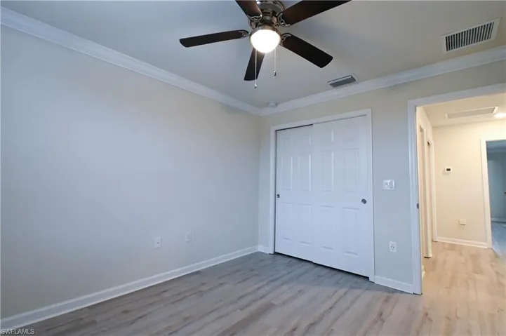 Unfurnished bedroom with ceiling fan, ornamental molding, a closet, and light wood-type flooring