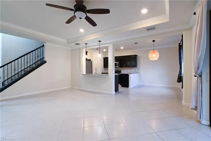 Unfurnished living room featuring light tile patterned floors, a tray ceiling, crown molding, sink, and ceiling fan