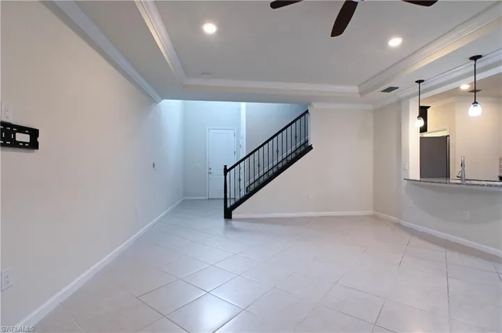 Unfurnished living room featuring crown molding, a raised ceiling, light tile patterned floors, and ceiling fan