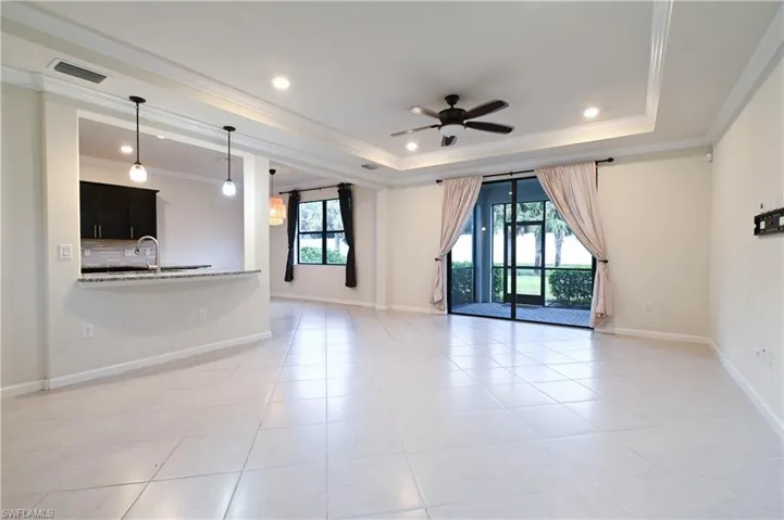 Unfurnished living room featuring light tile patterned floors, crown molding, sink, a tray ceiling, and ceiling fan