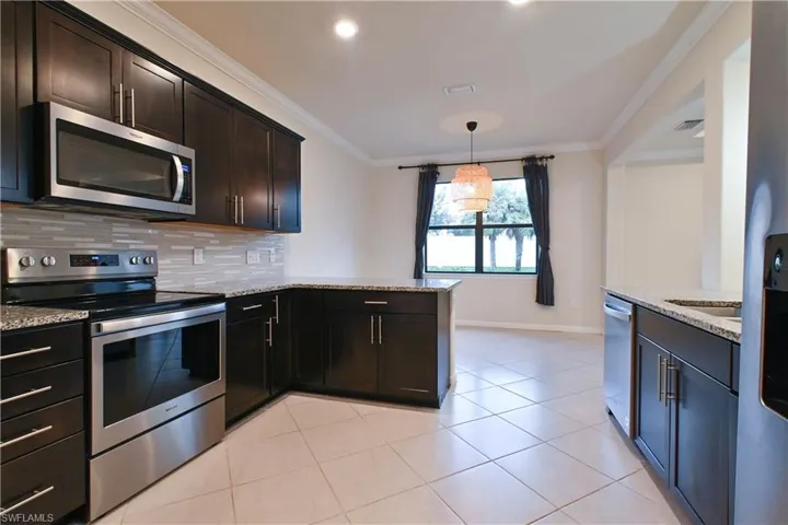 Kitchen featuring light tile patterned floors, stainless steel appliances, light stone counters, hanging light fixtures, and dark brown cabinetry