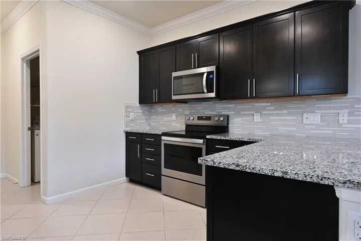 Kitchen featuring light tile patterned floors, backsplash, light stone countertops, and appliances with stainless steel finishes