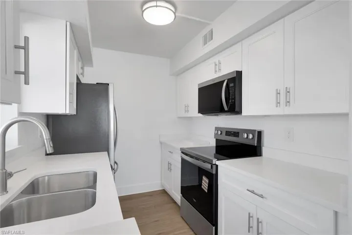 Kitchen featuring stainless steel appliances, white cabinetry, light wood finished floors, and light stone counters
