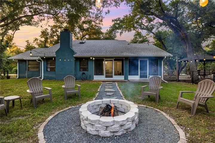 Back house at dusk featuring a lawn, a sunroom, and an outdoor fire pit