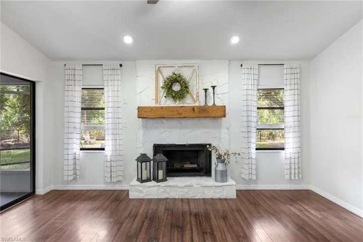 Unfurnished living room featuring a stone fireplace, dark hardwood / wood-style flooring, and a healthy amount of sunlight