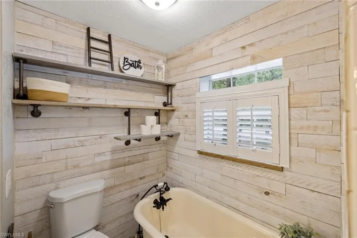 Bathroom featuring a bath, a textured ceiling, toilet, and wood walls
