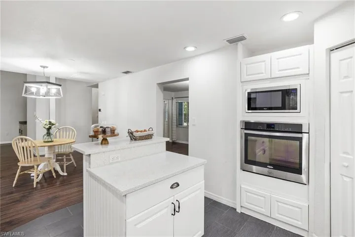 Kitchen with dark hardwood / wood-style floors, white cabinets, stainless steel appliances, and decorative light fixtures