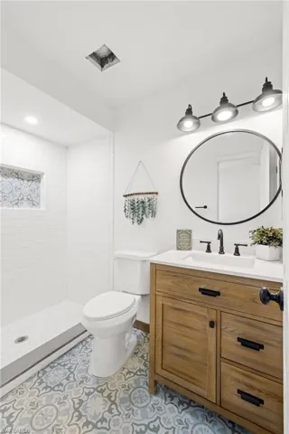 Bathroom featuring tile patterned floors, vanity, toilet, and a tile shower