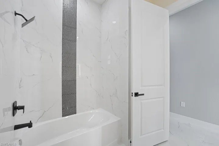 Bathtub featuring matte black fixtures, full-height white wall tile with a vertical mosaic inlay, and two-panel interior door