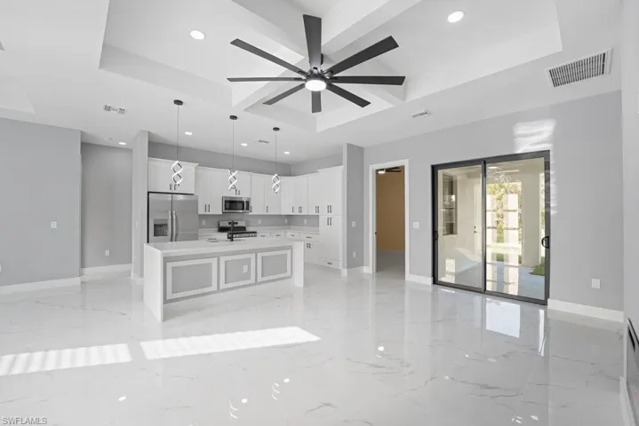 Kitchen featuring white cabinetry, center island with stone-finish countertop, recessed ceiling tray, large-format tile flooring, and sliding glass doors