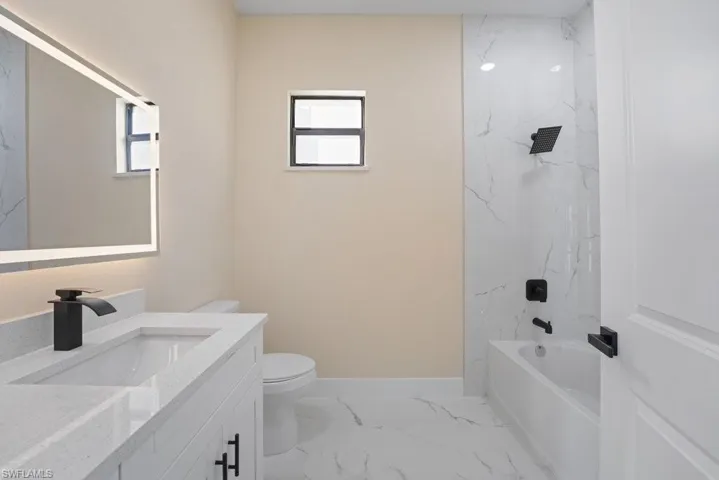 Bathroom featuring a vanity with a quartz countertop, integrated rectangular sink, matte black hardware, backlit mirror, and tub-shower combination with floor-to-ceiling tile surround