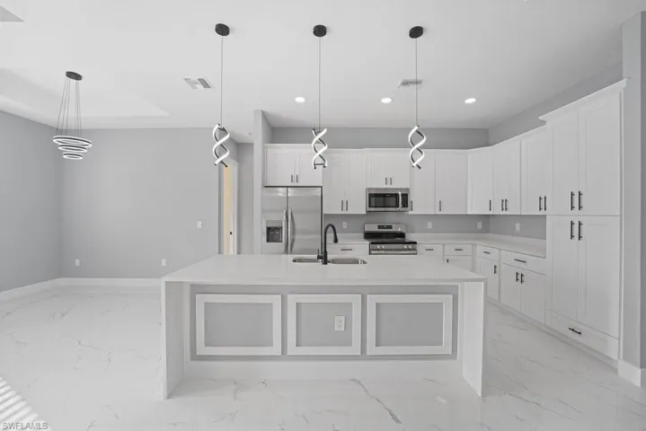 Kitchen featuring white shaker-style cabinetry, quartz countertops, a central island with panel detailing, stone-finish flooring, and contemporary spiral pendant lighting