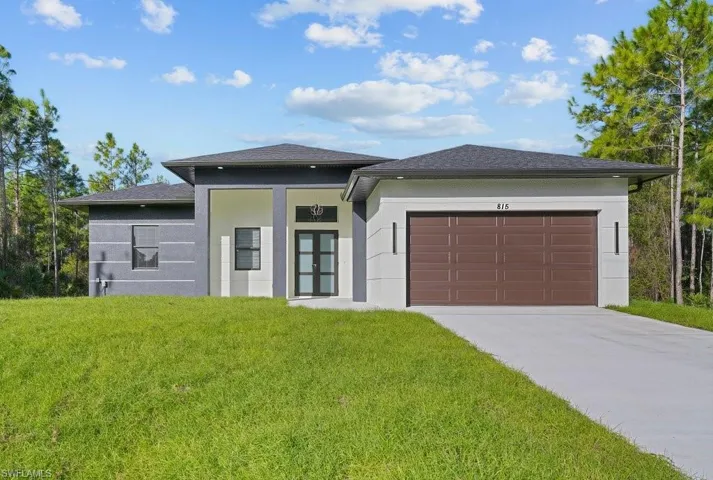 Contemporary single-story exterior featuring a high-contrast dark and light stucco facade, dual-tone roofline, solid-panel garage door, and recessed entryway with a multi-pane glass door