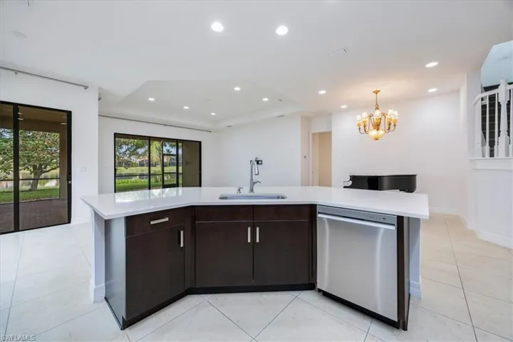 Kitchen with dishwasher, an inviting chandelier, a center island with sink, sink, and dark brown cabinets