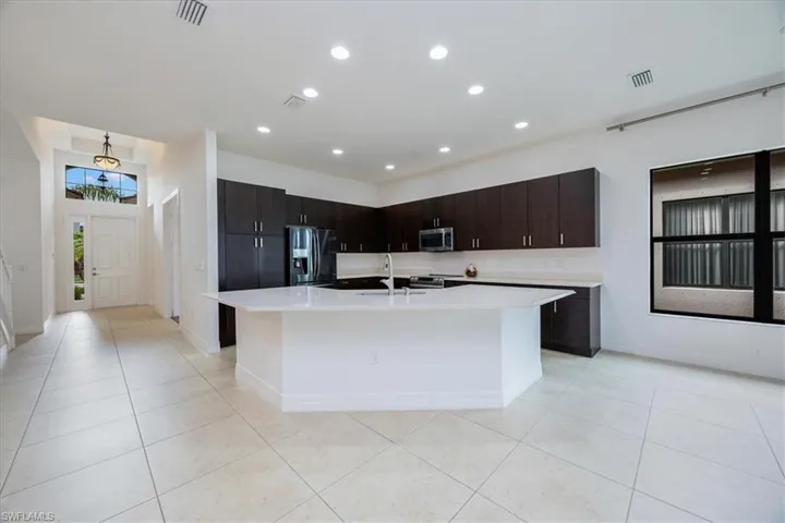 Kitchen featuring appliances with stainless steel finishes, dark brown cabinetry, a kitchen island with sink, sink, and light tile patterned floors