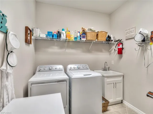 Clothes washing area featuring sink, cabinets, light tile floors, and separate washer and dryer