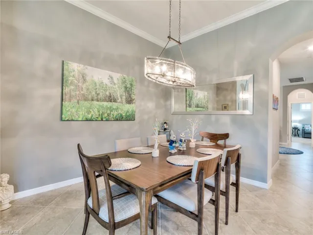 Dining space with ornamental molding, a chandelier, and light tile floors
