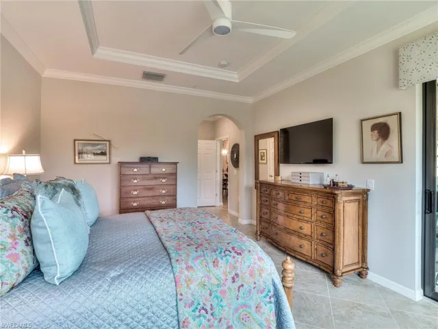 Bedroom featuring ornamental molding, light tile flooring, ceiling fan, and a raised ceiling