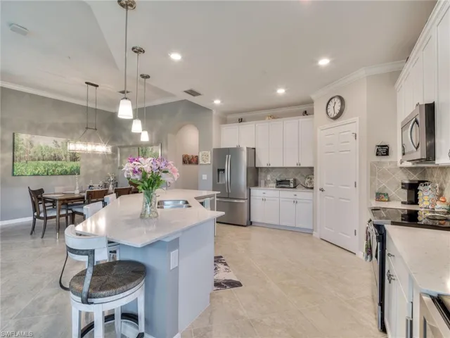 Kitchen with backsplash, hanging light fixtures, appliances with stainless steel finishes, and light stone counters