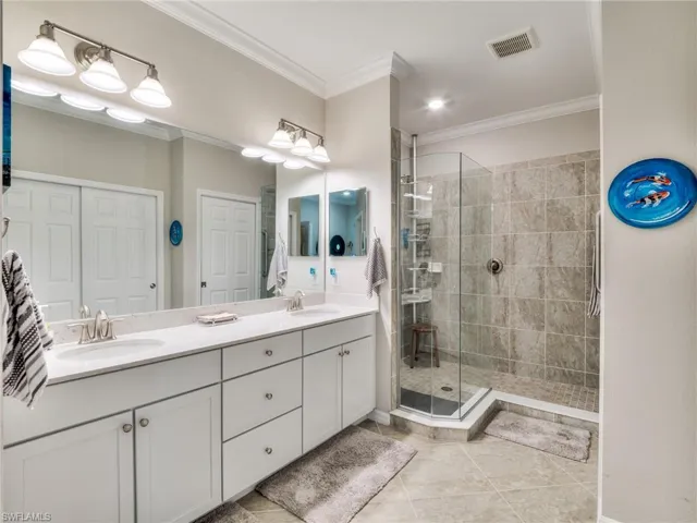 Bathroom featuring tile flooring, double sink, vanity with extensive cabinet space, a shower with shower door, and ornamental molding
