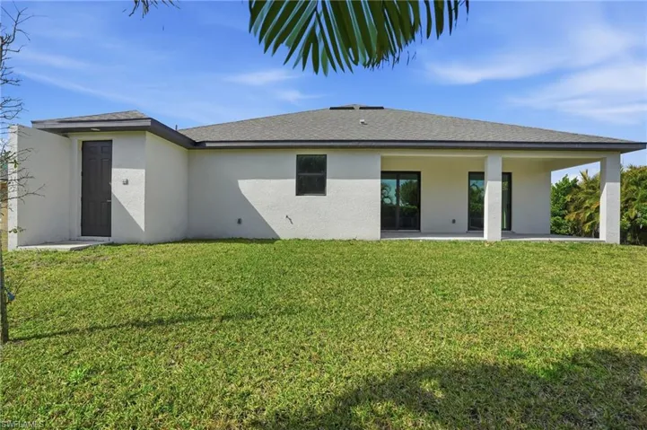 Back of house with a lawn, stucco siding, a patio, and a shingled roof