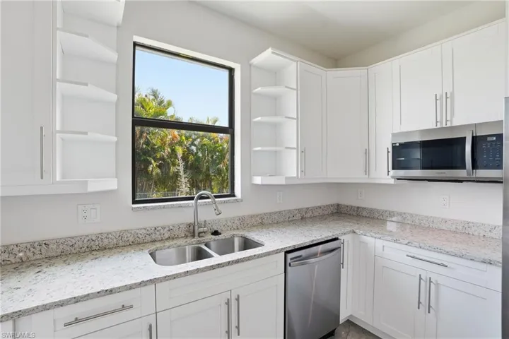 Kitchen featuring light stone countertops, open shelves, and stainless steel appliances