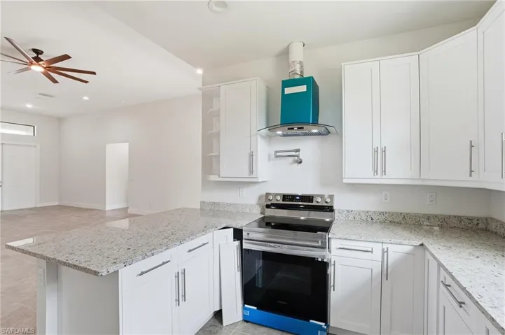 Kitchen with electric range, open shelves, white cabinets, light stone counters, and recessed lighting
