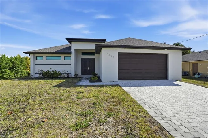 Prairie-style home featuring a front lawn, decorative driveway, stucco siding, a shingled roof, and an attached garage
