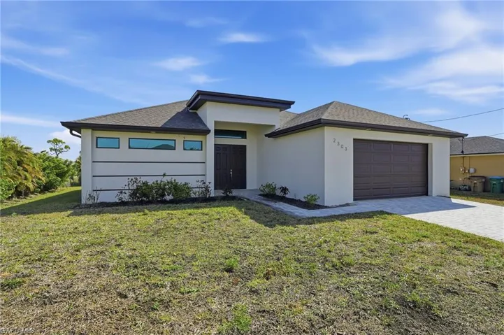 Prairie-style home featuring a front lawn, decorative driveway, stucco siding, a garage, and roof with shingles